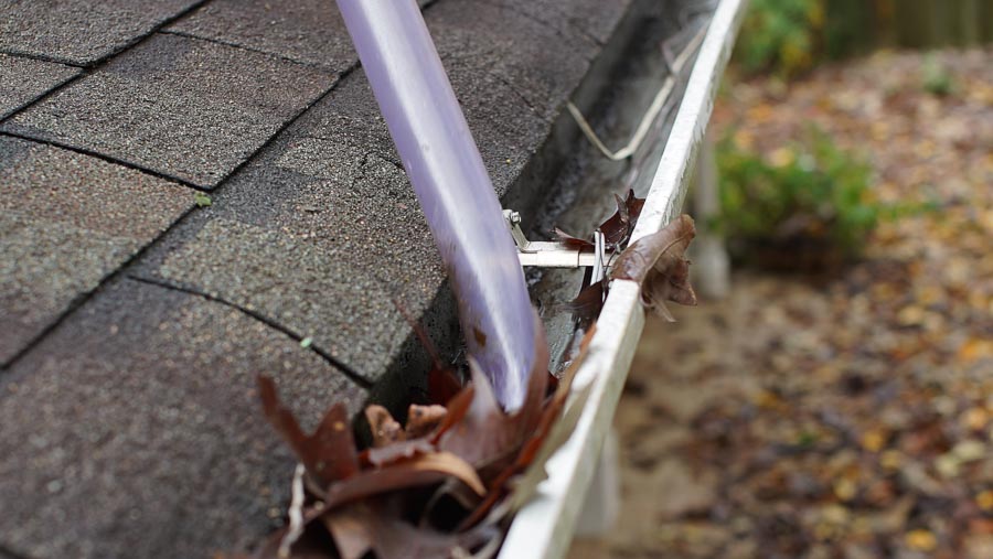 Close-up of a vacuum removing leaves and debris from a gutter on a residential home.