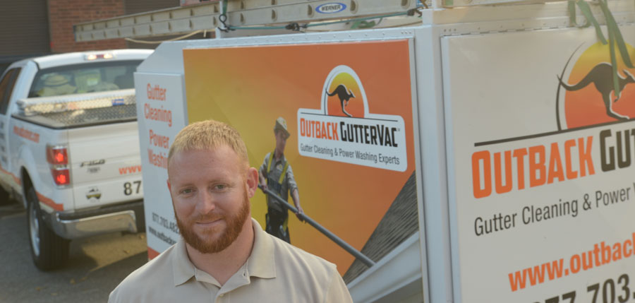 An Outback GutterVac smiles while standing in front of his branded pickup truck and equipment trailer.