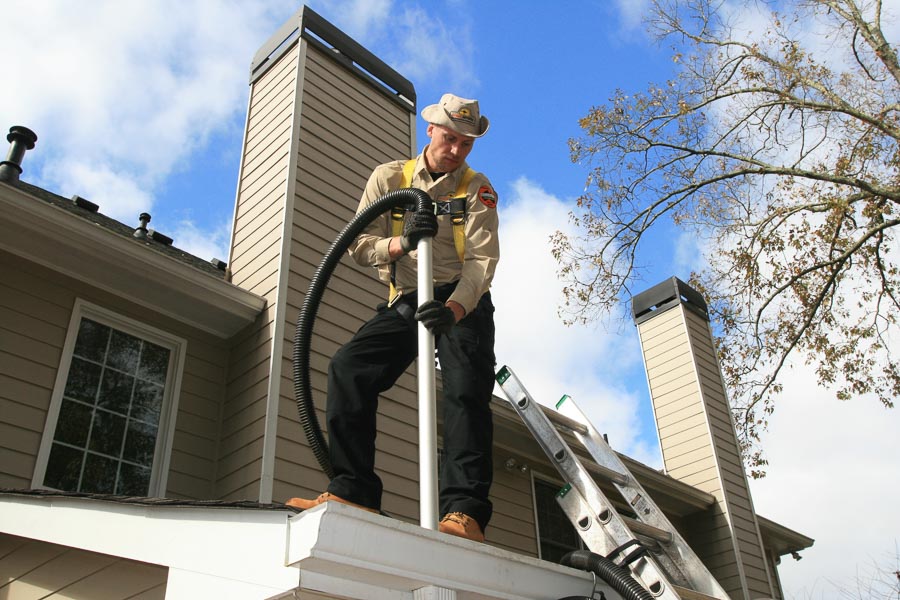 A technician uses the powerful ThunderVac to clean a gutter below him on a client’s roof.