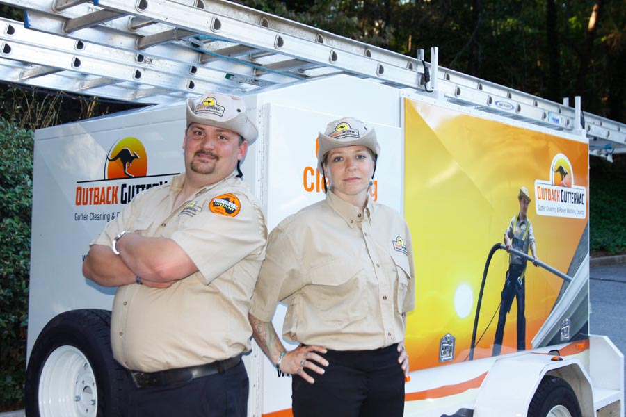 Two Outback GutterVac technicians stand in front of a ThunderVac trailer reflecting our current branding, with a ladder resting on top.