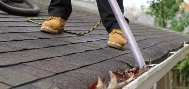 The lower legs and boots of a franchisee are visible on a rooftop as the franchisee vacuums leaves and other debris out of a client’s gutter.